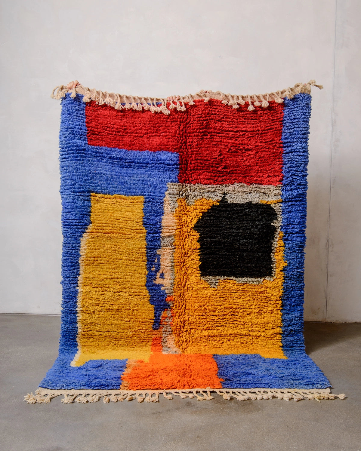 Berberlin vintage Berber rug being held up against white wall.